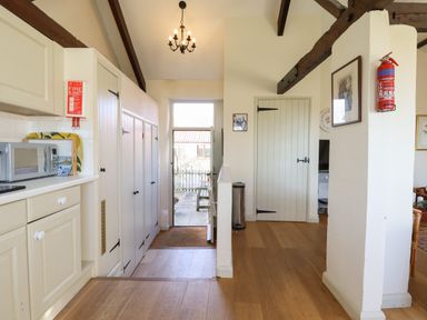 A kitchen with white cabinets microwave fire blanket and door leading outside at The Bull Pen in Colyton