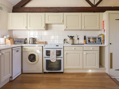A kitchen with white cabinets appliances a washing machine an oven a dishwasher and wooden flooring at The Bull Pen in Colyton