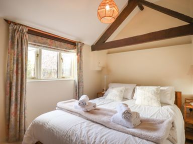 A bedroom with a bed with pillows blankets and rolled towels under a window with floral curtains at The Bull Pen in Colyton