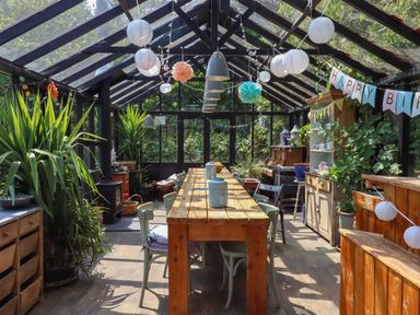 A sunroom with a long wooden table and chairs plants and birthday decorations at The Bull Pen in Colyton