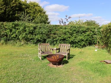 A garden with wooden chairs and a fire pit at The Bull Pen in Colyton