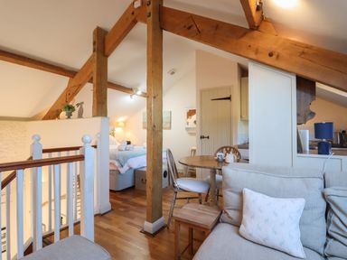 An open loft space with wooden beams a table with chairs a bed and a sofa at The Hay Loft in Colyton