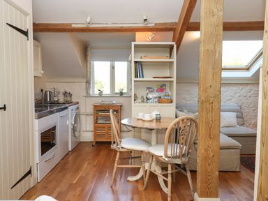 A kitchen and dining area with wooden floor and furniture including a round table with chairs a washing machine and a sofa at The Hay Loft in Colyton
