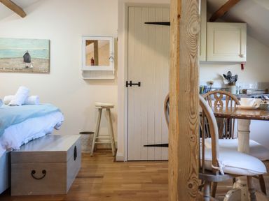 A bedroom and kitchen area with a bed, dining table with chairs, wooden pillar, and a door at The Hay Loft in Colyton
