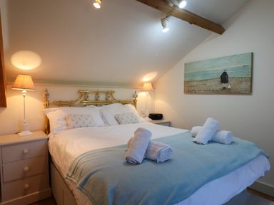 A bedroom with a double bed with white linens and rolled towels on a blue blanket at The Hay Loft in Colyton