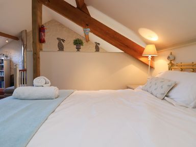 A bedroom with a bed with white sheets and rolled towels under a wooden ceiling beam at The Hay Loft in Colyton