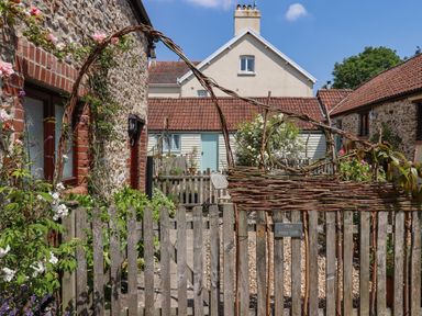 A garden area with a wooden gate and vine decorations outside stone cottages at The Hay Loft in Colyton