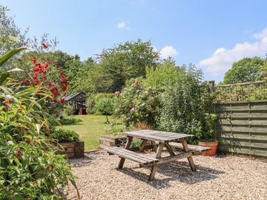 A garden with a wooden picnic table gravel area flowering plants and a greenhouse in the background at The Hay Loft in Colyton
