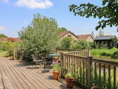 A wooden deck with chairs and potted plants surrounded by greenery and buildings at The Hay Loft in Colyton