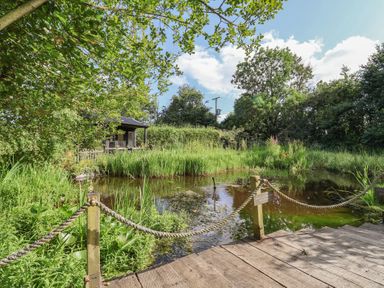 A garden with a pond and wooden deck at The Hay Loft in Colyton