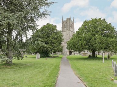 A church with a clock tower and pathway surrounded by grass trees and gravestones at The Old Bakehouse in Avebury
