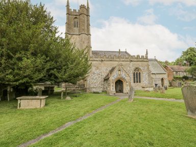 An old stone church with a clock tower surrounded by grass and gravestones