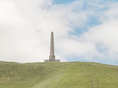 An obelisk monument on top of a grassy hill under a partly cloudy sky at The Old Bakehouse in Avebury