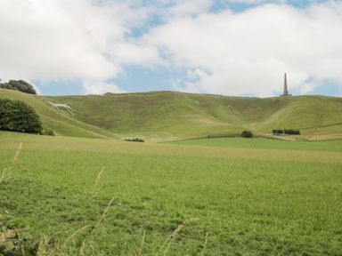 A green hill with a large horse figure carved into the hillside and an obelisk monument in the distance at The Old Bakehouse in Avebury