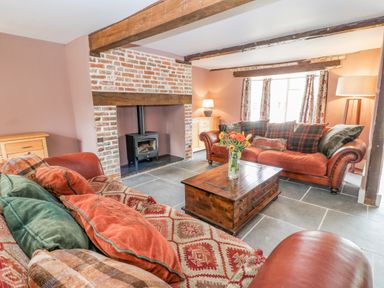 A living room with two sofas a wooden coffee table a brick fireplace with a wood stove and exposed ceiling beams at The Old Bakehouse in Avebury