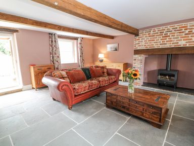 A living room with a red sofa wooden coffee table with flowers wood burning stove and exposed wooden ceiling beams at The Old Bakehouse in Avebury
