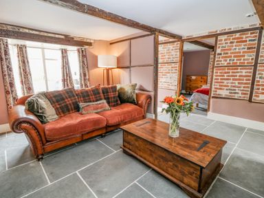 A living room with a brown leather sofa pillows wooden coffee table and flowers on table at The Old Bakehouse in Avebury