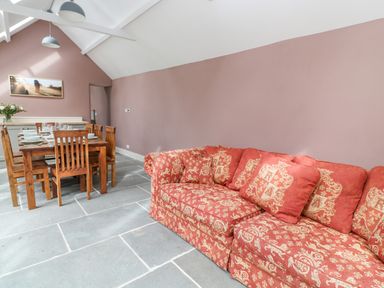 A dining area with a wooden table set for six and a patterned red sofa against a pink wall at The Old Bakehouse in Avebury