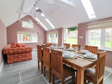 A dining area with a wooden table set for eight and a patterned sofa by windows at The Old Bakehouse in Avebury