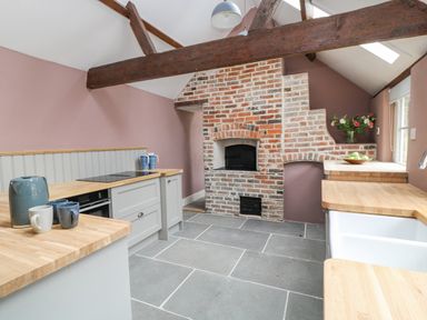 A kitchen with wooden countertops a brick oven exposed ceiling beams and a vase of flowers at The Old Bakehouse in Avebury