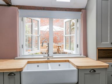 A kitchen sink with a faucet under a window showing an outdoor dining area with a table chairs and an umbrella at The Old Bakehouse in Avebury