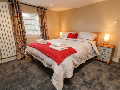 A bedroom with a bed covered with white bedding and a red throw and two bedside tables with lamps at The Old Bakehouse in Avebury
