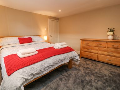 A bedroom with a bed, wooden dresser, towels, and a vase with flowers at The Old Bakehouse in Avebury