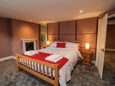 A bedroom with a wooden bed white and red bedding two bedside tables with lamps and a fireplace at The Old Bakehouse in Avebury