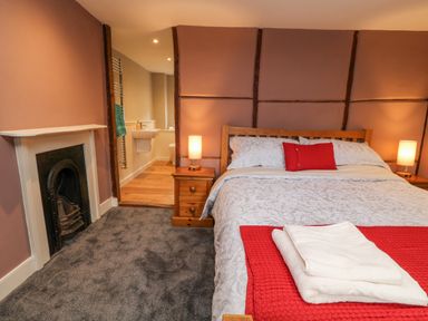 A bedroom with a bed covered with white and red linens beside two wooden nightstands and a fireplace at The Old Bakehouse in Avebury