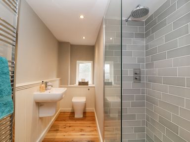 A bathroom with a wall-mounted sink toilet wooden floor and a tiled shower at The Old Bakehouse in Avebury