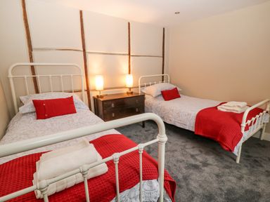A bedroom with two single beds with red cushions and blankets and a wooden chest of drawers with two lamps at The Old Bakehouse in Avebury
