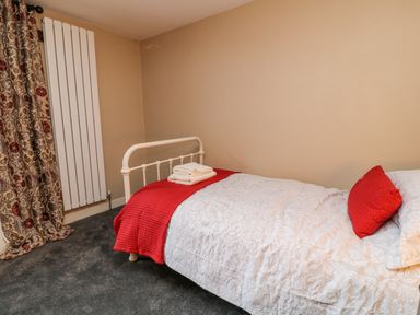 A bedroom with a single bed covered in white bedding and a red pillow and blanket next to patterned curtains at The Old Bakehouse in Avebury