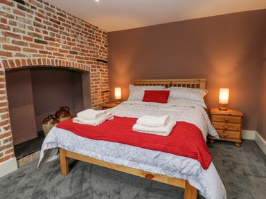 A bedroom with a wooden bed with red and white bedding and a brick fireplace at The Old Bakehouse in Avebury