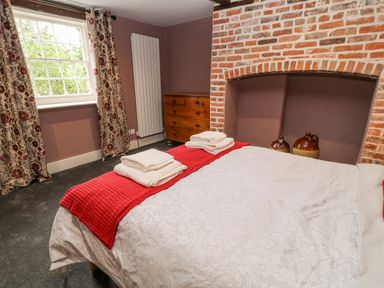 A bedroom with a bed with folded towels on it a brick fireplace a wooden chest of drawers and floral curtains at The Old Bakehouse in Avebury