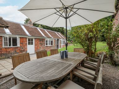 A wooden outdoor dining table with chairs and an umbrella next to a brick house at The Old Bakehouse in Avebury