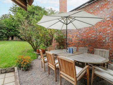 An outdoor patio with a wooden dining table and chairs under a large white umbrella next to a brick wall with a garden in the background at The Old Bakehouse in Avebury