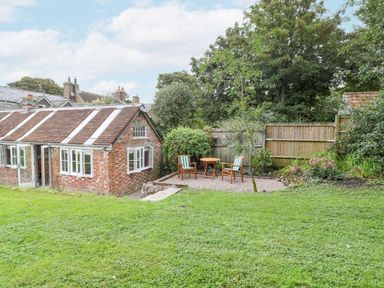 An outdoor garden area with a brick house a small patio with two chairs and a table and a grassy lawn at The Old Bakehouse in Avebury