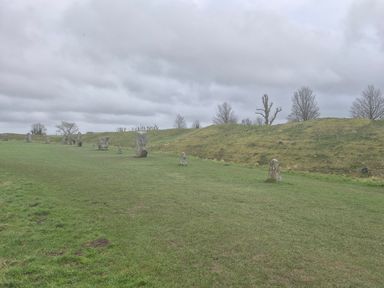 A grassy field with standing stones and a small hill under a cloudy sky at The Old Bakehouse in Avebury