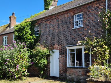 A brick house with a white door and windows and plants growing around it at The Old Bakehouse in Avebury