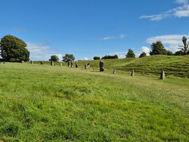 A grassy field with standing stones and trees under a blue sky at The Old Bakehouse in Avebury