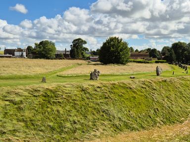 A grassy field with standing stones and houses in the background at The Old Bakehouse in Avebury