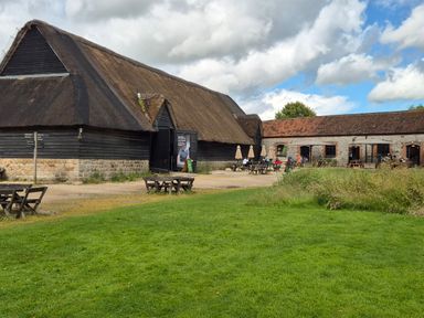 An outdoor area with wooden benches and tables near thatched and brick buildings under a partly cloudy sky at The Old Bakehouse in Avebury