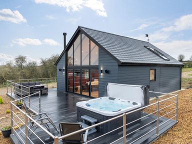A modern house with a large glass front and dark wood deck with hot tub and outdoor seating at Stags Mount in Thornton Dale