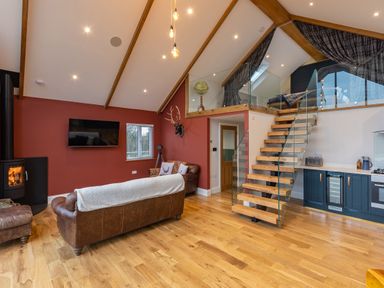 A living room with brown leather sofas a wood stove and a staircase leading to a loft at Stags Mount in Thornton Dale