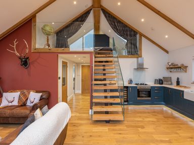 An open living space with a staircase leading to a loft bedroom and a kitchen with blue cabinets at Stags Mount in Thornton Dale