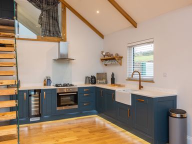 A kitchen with dark blue cabinets a gas stove an oven a white farmhouse sink and wooden stairs at Stags Mount in Thornton Dale
