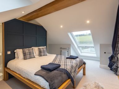 A bedroom with a wooden bed with plaid pillows and blanket near a slanted window at Stags Mount in Thornton Dale