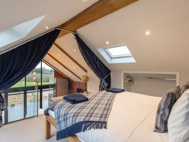 A loft bedroom with a bed, plaid blanket, pillows, skylight, and glass railing at Stags Mount in Thornton Dale