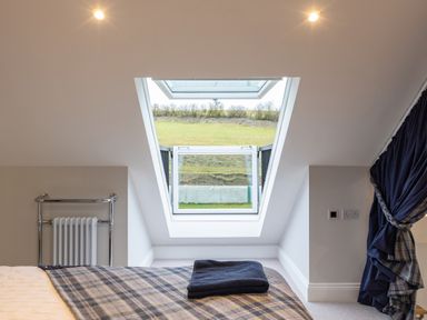 A bedroom with a bed covered in a plaid blanket and towels near a large open skylight window with a view of grass at Stags Mount in Thornton Dale