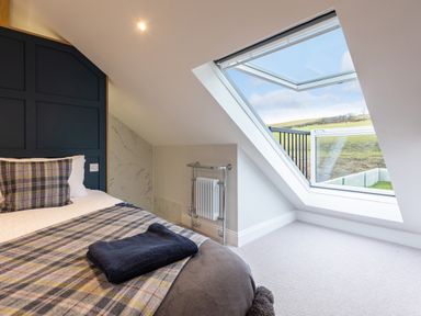 A bedroom with a bed near a slanted window showing an outdoor view at Stags Mount in Thornton Dale